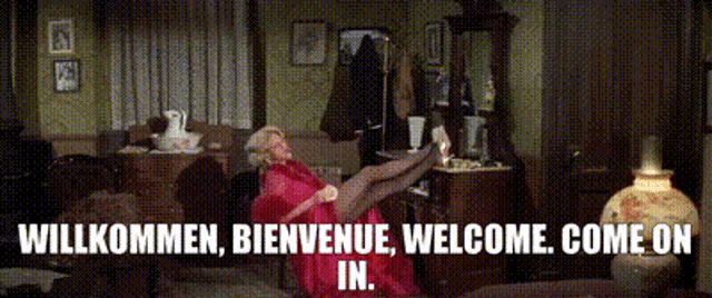a woman in a red dress is sitting on a couch with the words willkommen bienvenue welcome come on in