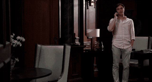 a man in a pink shirt is talking on a cell phone in a dark room