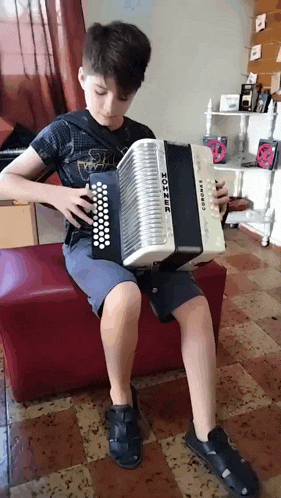 a young boy is playing an accordion while sitting on a red couch