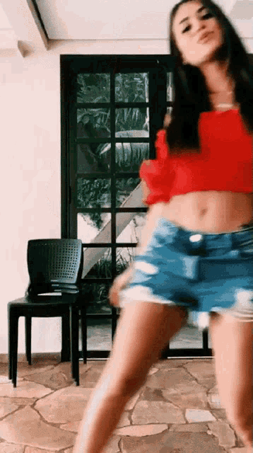 a woman in a red crop top and shorts is dancing in a room .