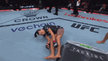 a woman laying on a wrestling mat with ufc taurine and crown vechain written on the floor