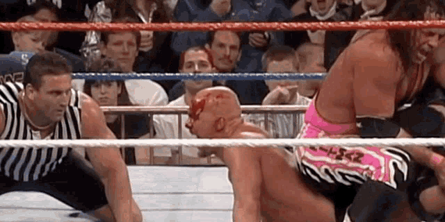 two wrestlers are fighting in a ring with a referee in the background .