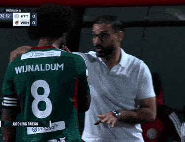 a man in a white shirt is talking to a soccer player in a green jersey with the number 8 on it