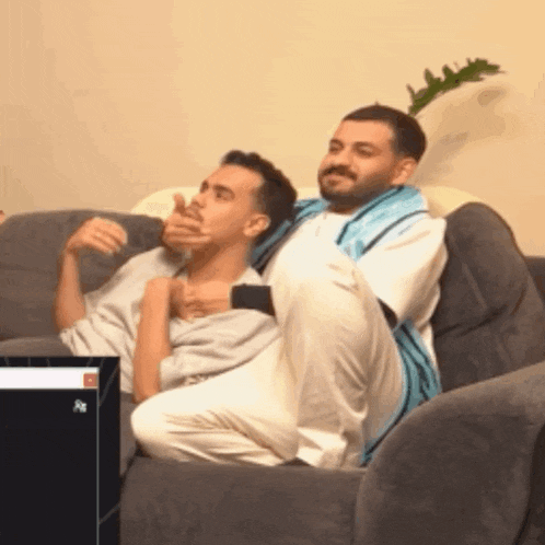 two men are sitting on a couch and one of them is covering his mouth