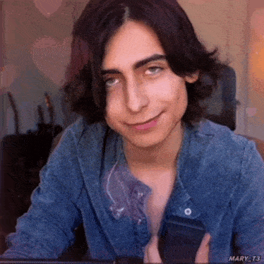 a young man in a denim jacket is smiling and holding a cell phone .