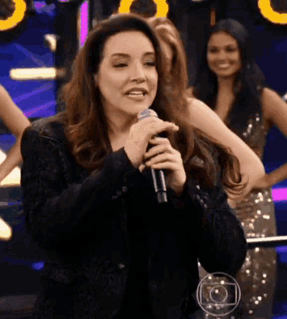 a woman singing into a microphone in front of a group of girls