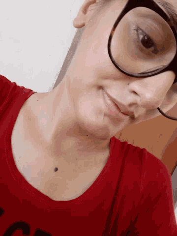 a woman wearing glasses and a red shirt has a black spot on her chest