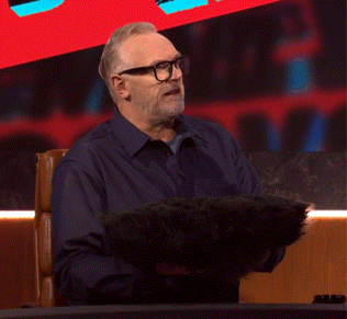 a man with glasses and a beard is sitting at a desk holding a black object