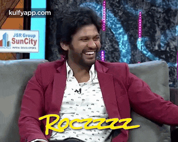 a man in a pink jacket is sitting on a couch laughing .