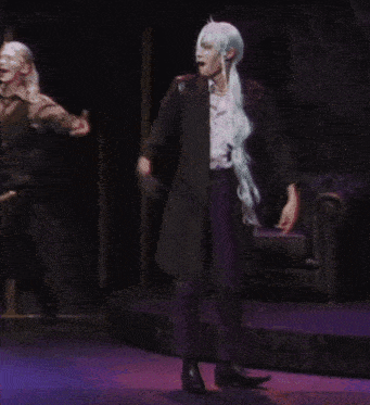 a man with long blue hair is dancing on stage