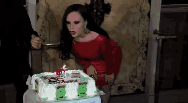 a woman in a red dress blows out a candle on a cake with the number 50 on it