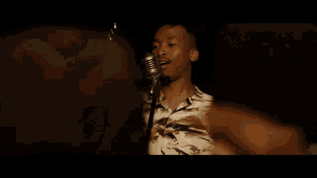 a man is singing into a microphone while standing in front of a crowd .