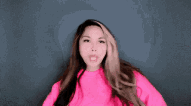 a woman with long hair is wearing a pink sweater and making a funny face