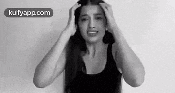 a black and white photo of a woman holding her head with her hands .