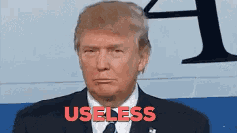 donald trump is wearing a suit and tie and has the word useless written in red on his face .