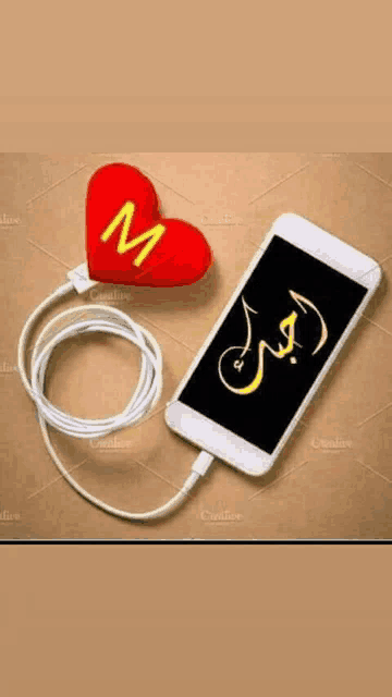 a red heart with the letter m on it next to a cell phone with a cord attached to it .