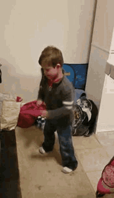 a young boy is standing on a tiled floor in a room holding a bottle .