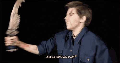 a man in a blue shirt is holding a feather in his hand and says `` shake it off ! shake it off ! ''
