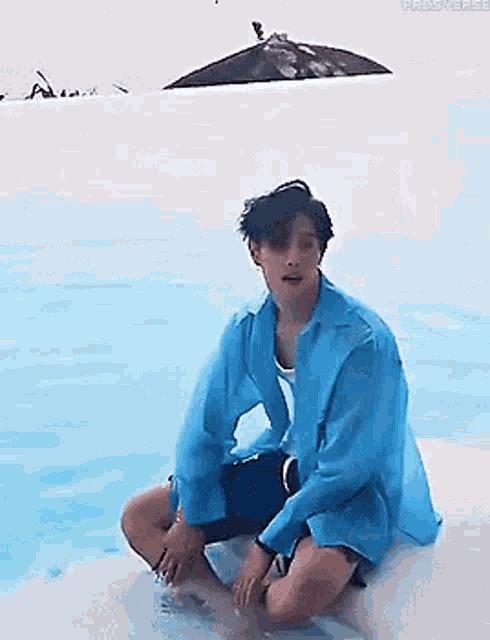 a man in a blue shirt is sitting on a rock near a swimming pool .