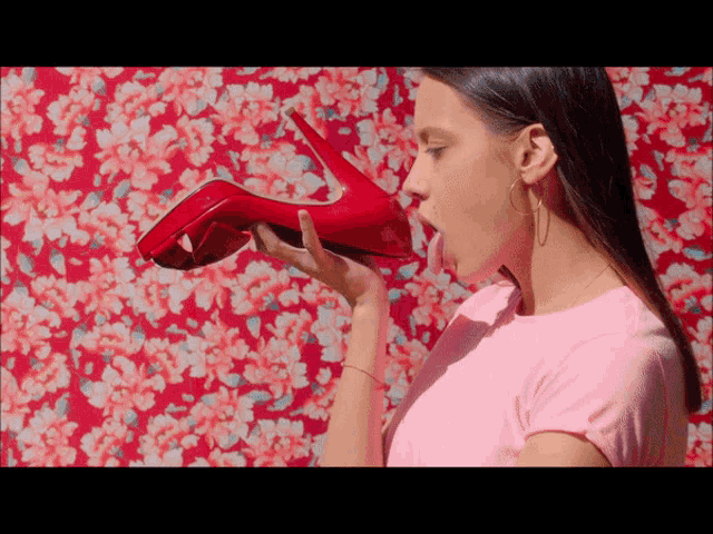 a woman in a pink shirt is licking a red high heel shoe