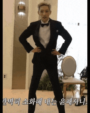 a man in a tuxedo is standing with his hands on his hips in a room