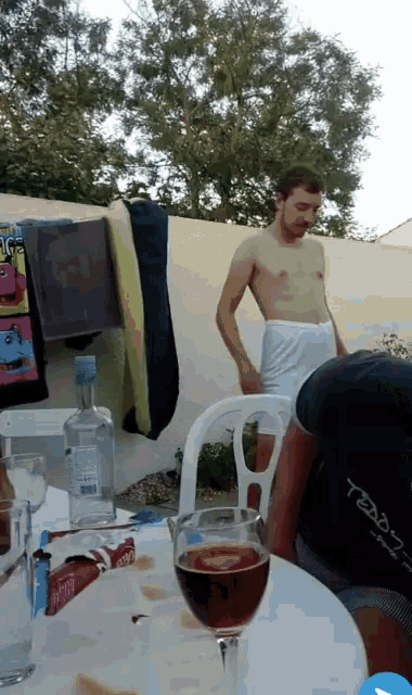 a man with a towel around his waist is standing in front of a table with a glass of wine