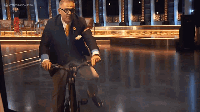 a man in a suit and tie is riding a bicycle with the hashtag #adricdragonsdev on the bottom of the screen