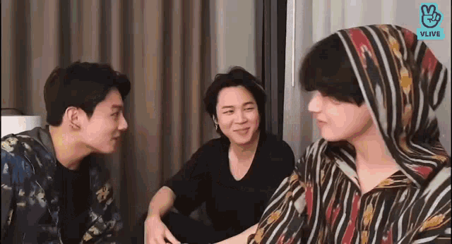 a group of three men are sitting next to each other in a room and talking to each other .