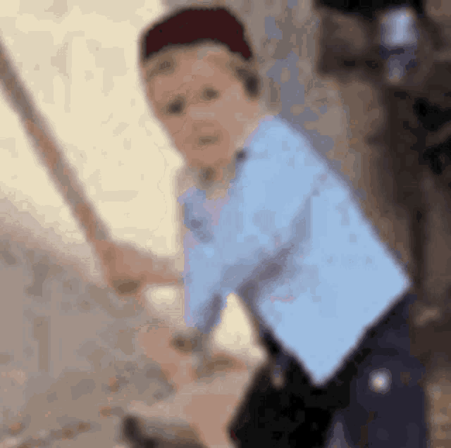 a blurry picture of a young boy wearing a blue shirt and a red hat holding a sword .