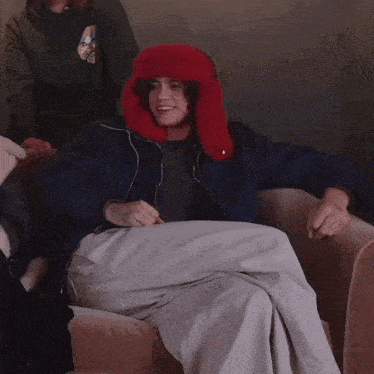 a man wearing a blue jacket and a red hat is sitting on a couch