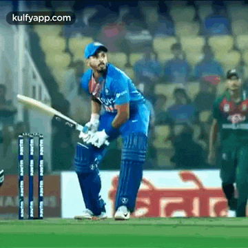 a cricket player is swinging a bat at a ball while another player watches .