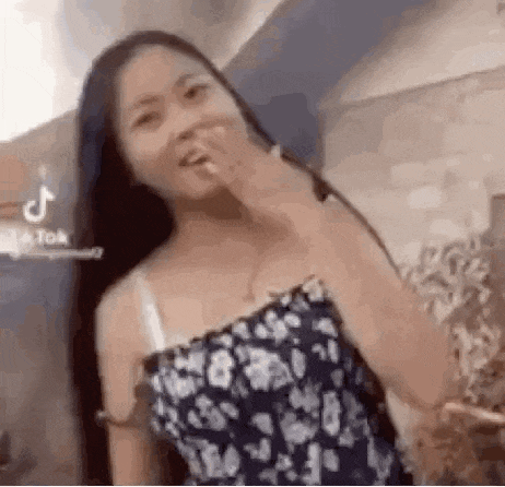a woman with long hair is covering her mouth with her hand while wearing a floral dress .