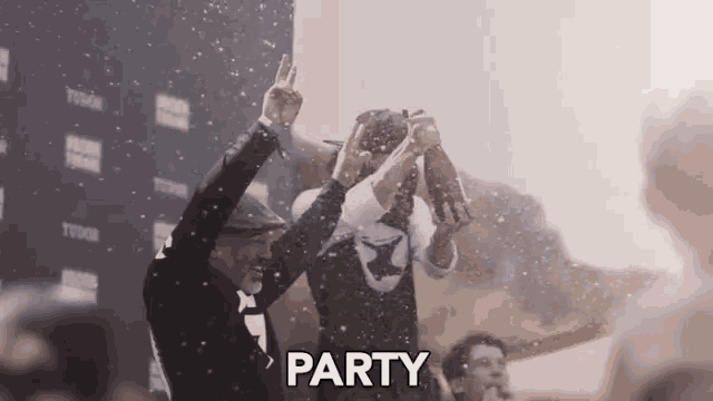 two men are standing next to each other with their arms in the air and the word party is being thrown in the air .