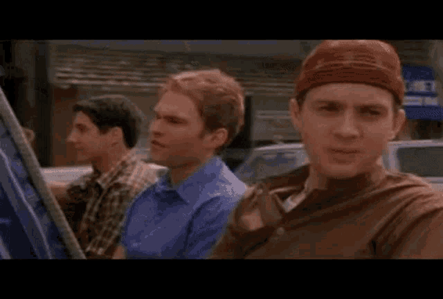 three men are sitting in a car and one of them is wearing a headband