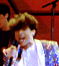 a woman singing into a microphone in front of a red background