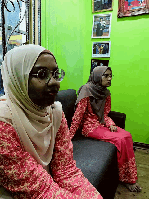 two women wearing hijabs and glasses sit on a couch