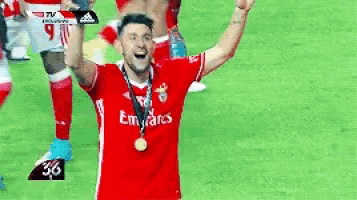 a soccer player wearing a red emirates shirt is raising his arms in the air .