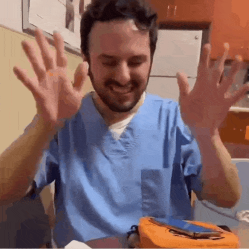 a man in a blue scrub top is smiling and waving