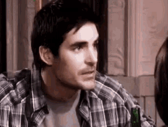 a man in a plaid shirt is sitting at a table with a bottle of beer in front of him .