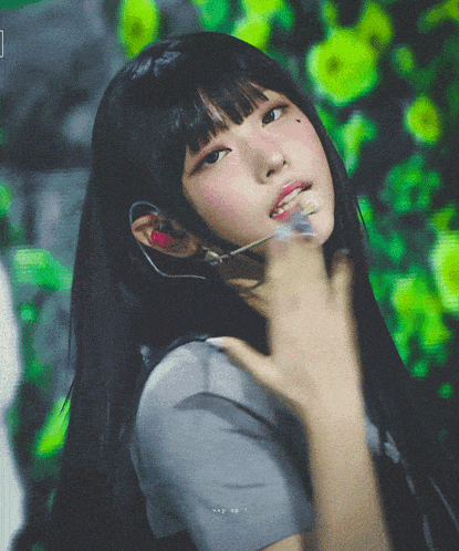 a girl with long black hair is wearing a gray shirt and a microphone in her ear