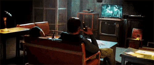 a man is sitting on a couch in front of a television while drinking a beer .