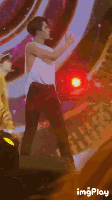 a man in a white shirt is dancing on a stage while another man in a yellow shirt watches