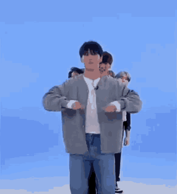 a man in a gray jacket and jeans is dancing in front of a blue background .