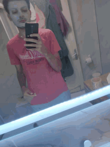 a man taking a picture of himself in a mirror wearing a shirt that says ' essential fitness '