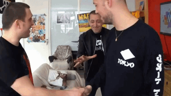 a man wearing a black tokyo shirt shakes hands with two other men