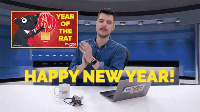 a man sitting at a desk with a laptop and a sign that says happy new year