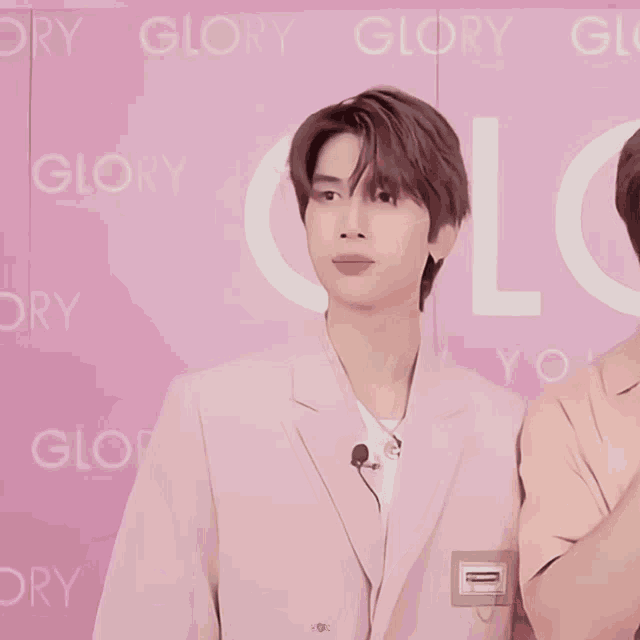 a man in a pink suit stands in front of a pink wall that says glory