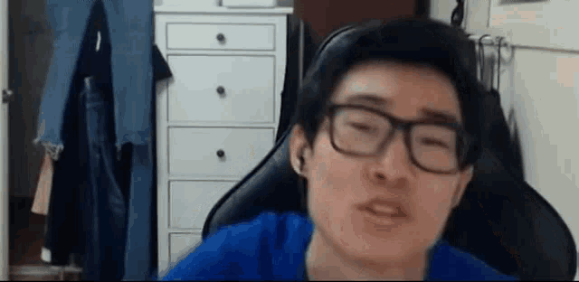 a man wearing glasses and ear buds is sitting in a chair in a room .