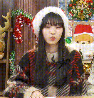 a girl wearing a santa hat and a plaid sweater is blowing a kiss .