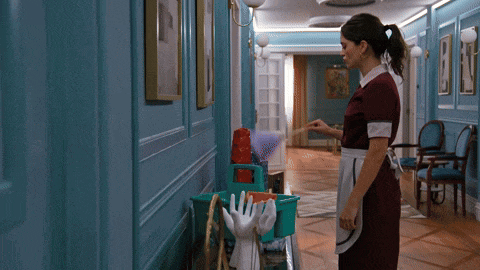 a maid is standing in a hallway with a mop bucket and gloves